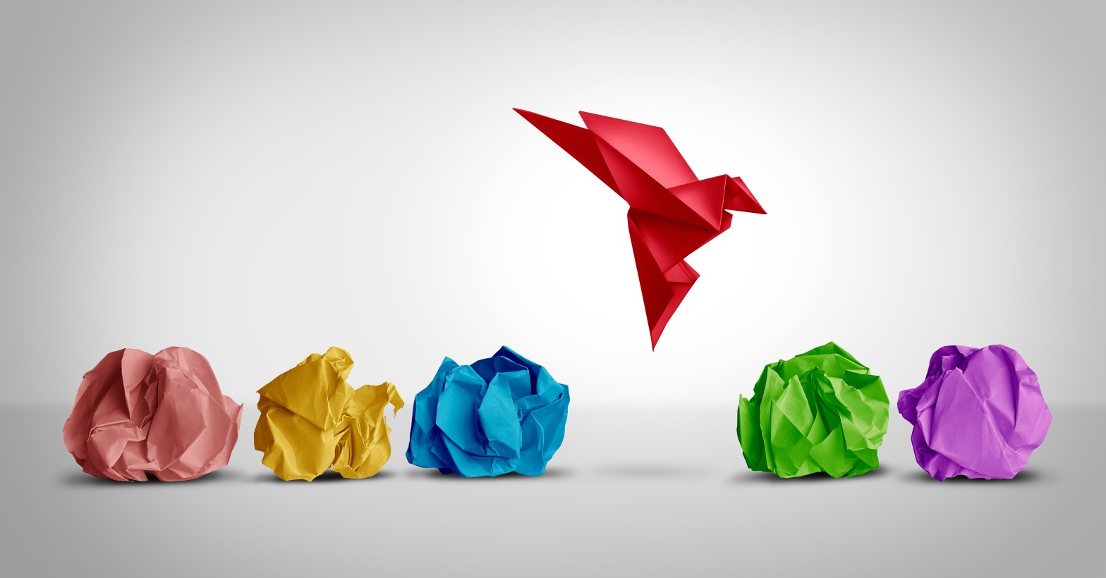 Crumpled pieces of paper litter the ground, as a successfully folded paper crane floats above.